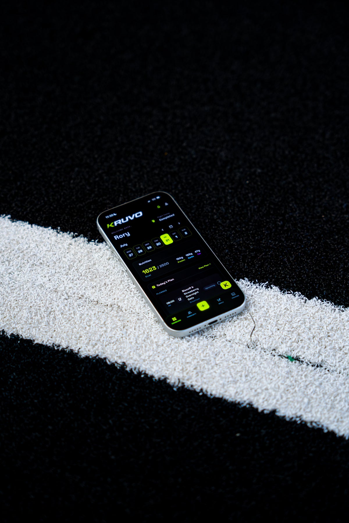 Phone showing the KRUVO app lying on dark gym turf beside a white line