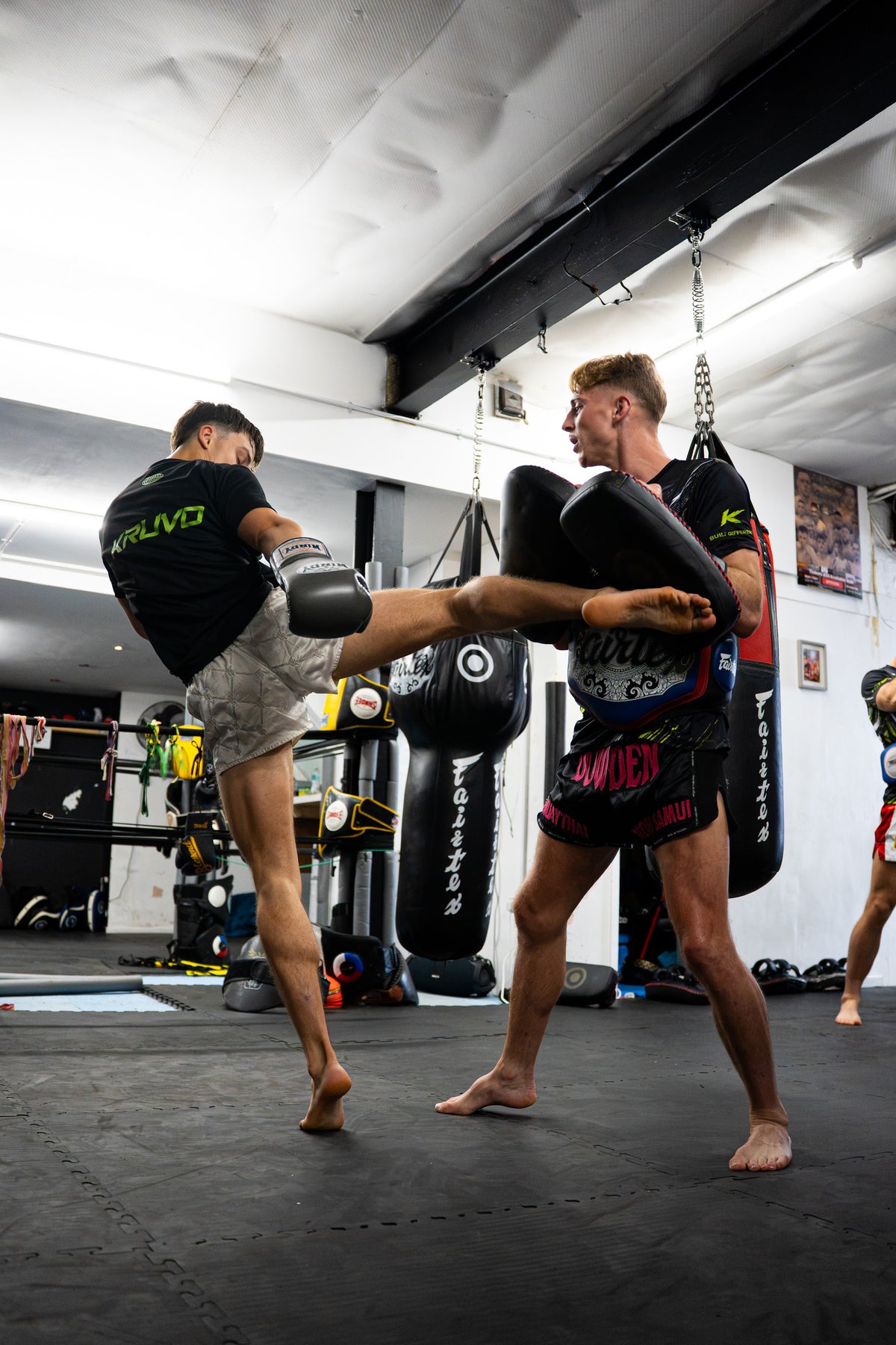 Fighter in a KRUVO tee landing a kick on pads in the gym